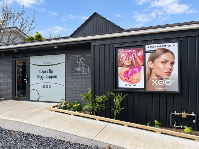 Dark salon frontage with Unique Hair & Beauty identification and colourful beauty-service window graphics.